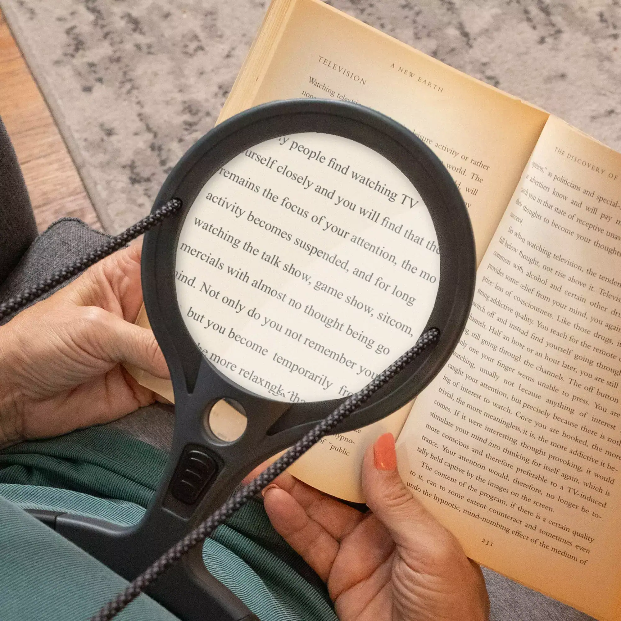Una persona usa la Lupa manos libres con LED COB Carson AS-70 | Serie Lume™ 2x con lente de 4,3" (11 cm), cómoda y de alta claridad, para leer un libro cómodamente en su regazo.