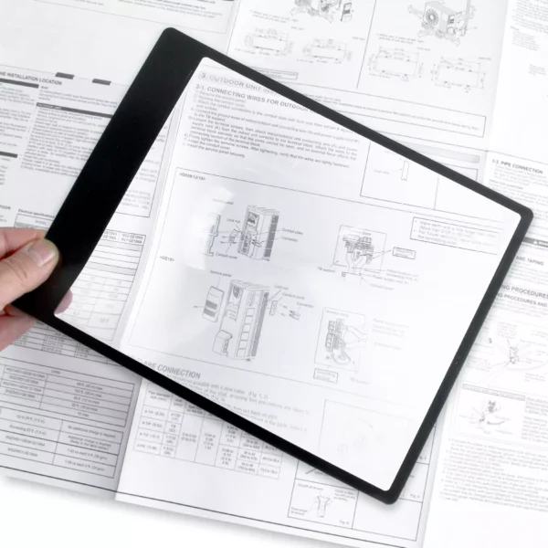 Una mano sostiene la lupa de hoja flexible con marco Carson DM-11 | 2x tipo Fresnel sobre documentos técnicos, ampliando diagramas y texto para lectura cómoda en libros, prensa y revistas.