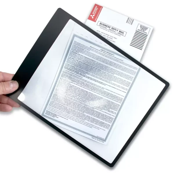 Una mano sostiene la lupa de hoja flexible con marco Carson DM-11 | 2x tipo Fresnel sobre un documento, ampliando el texto impreso. En el fondo se ve parcialmente un sobre "Correo de respuesta comercial".