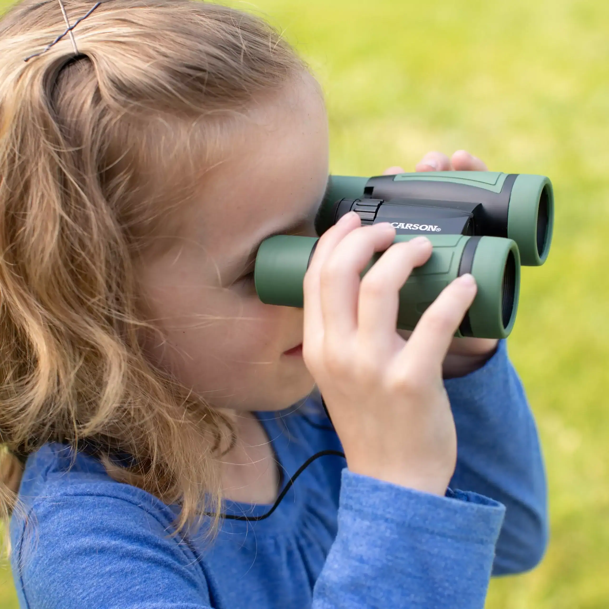 Un niño con camiseta azul usa los Prismáticos infantiles Carson HU-530 | Serie Hawk™ de 30 mm y diseño resistente para observación al aire libre, disfrutando en un entorno de césped.