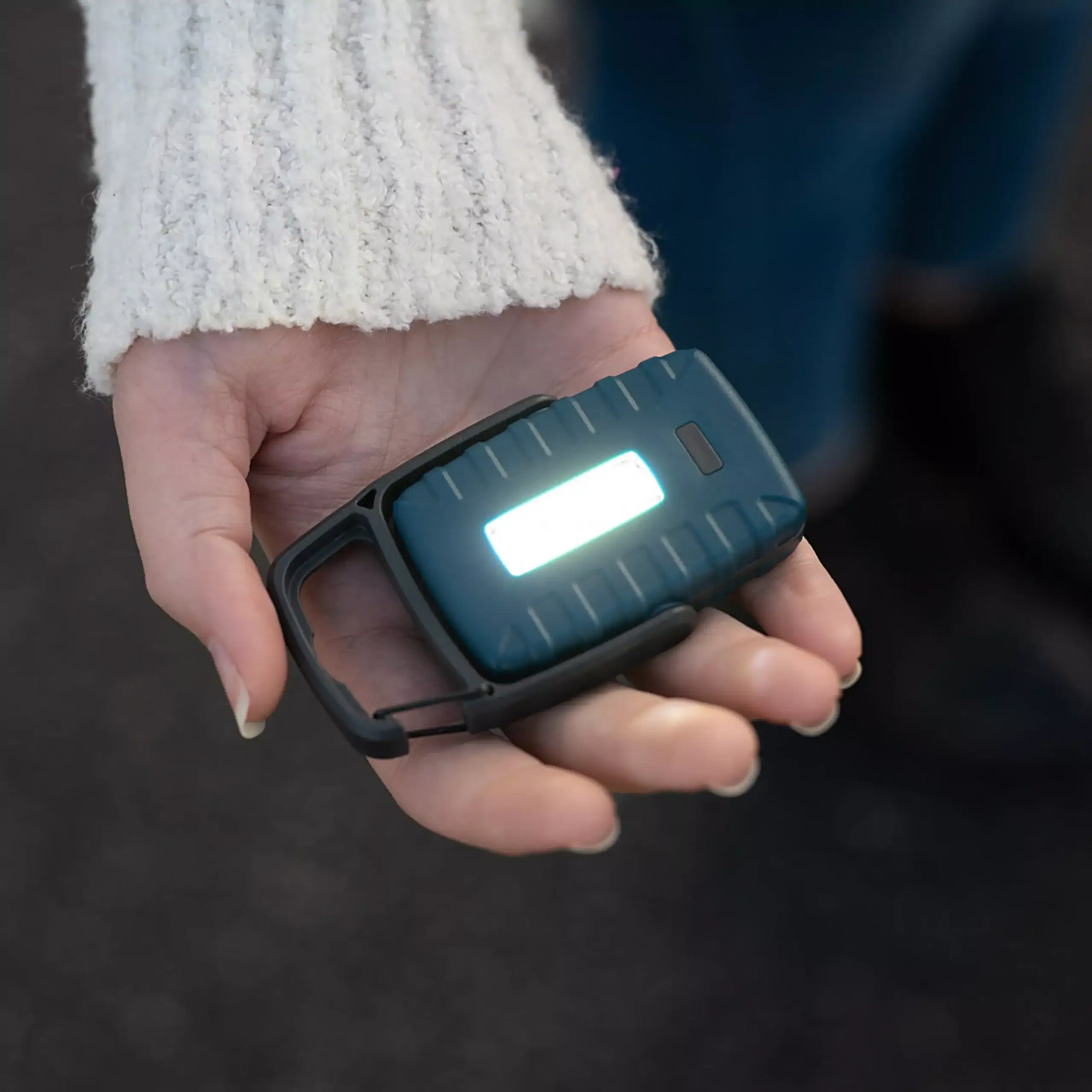 Una persona con manga tejida blanca sostiene en la mano la Linterna LED COB multipropósito Carson KL-20, compacta y equipada con luz blanca y roja, 4 modos, gancho y soporte integrado, ideal para múltiples usos.