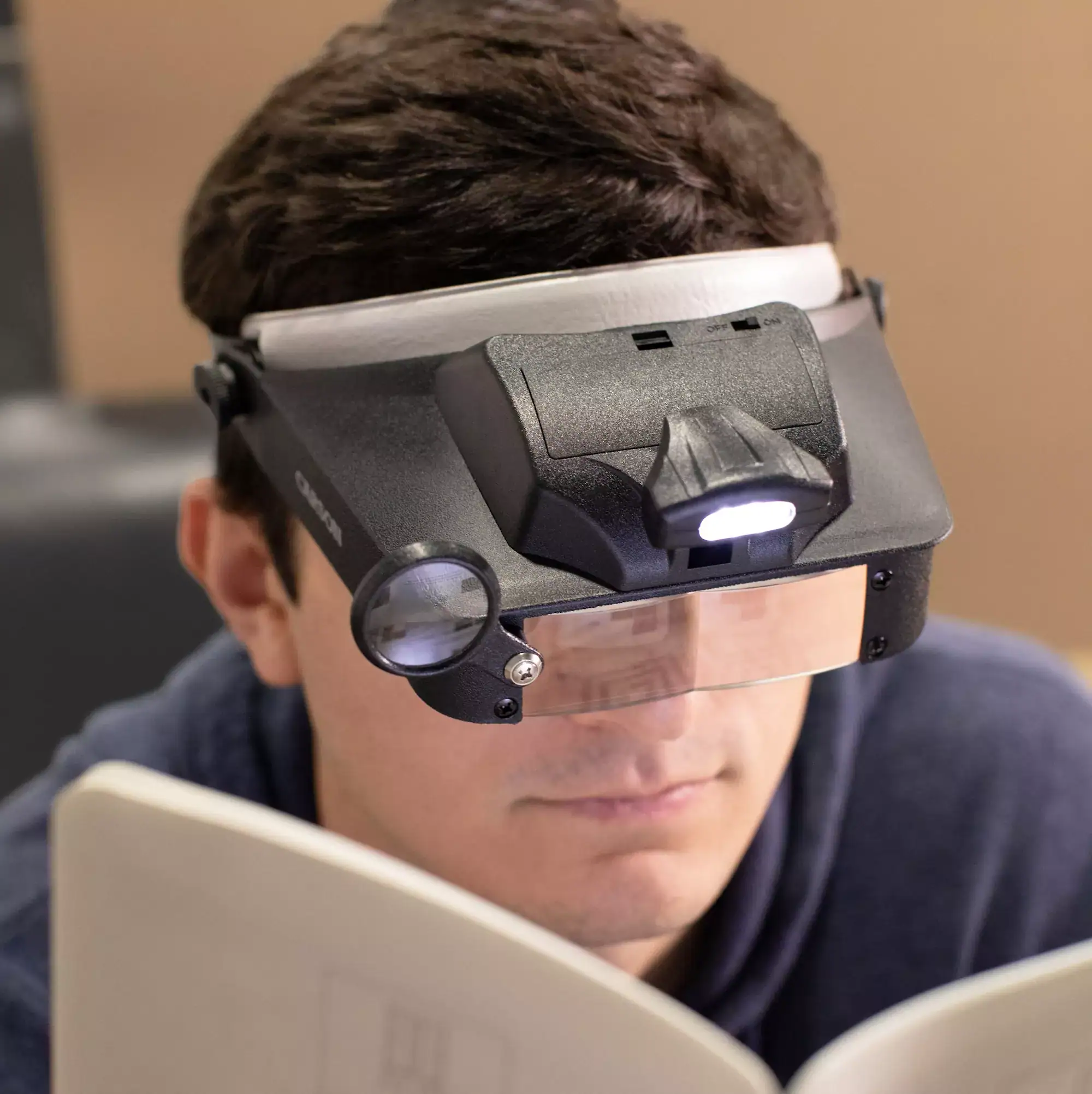Alguien usa la Lupa de cabeza manos libres con LED Carson LV-10 | Serie LumiVisor™ con aumento intercambiable de 2x/3x/5x/6x y correa ajustable mientras lee un libro.