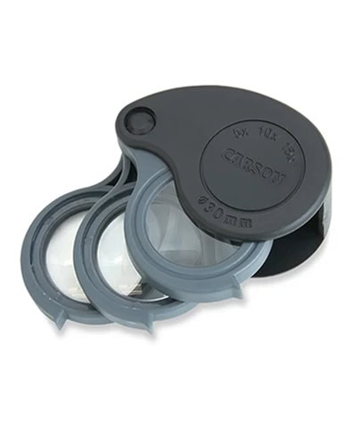 Una lupa plegable compacta con tres lentes redondas en un estuche de plástico gris y negro, etiquetada con detalles de aumento.