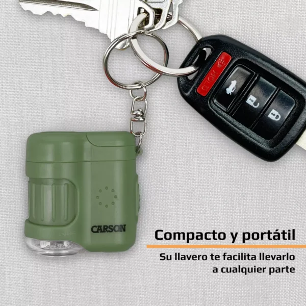 El Microscopio de bolsillo Carson MM-280G MicroMini™ 20x verde, con luz UV y linterna LED, aparece sujeto a un llavero con llaves y control, sobre tela gris clara. Un texto en español destaca su portabilidad.