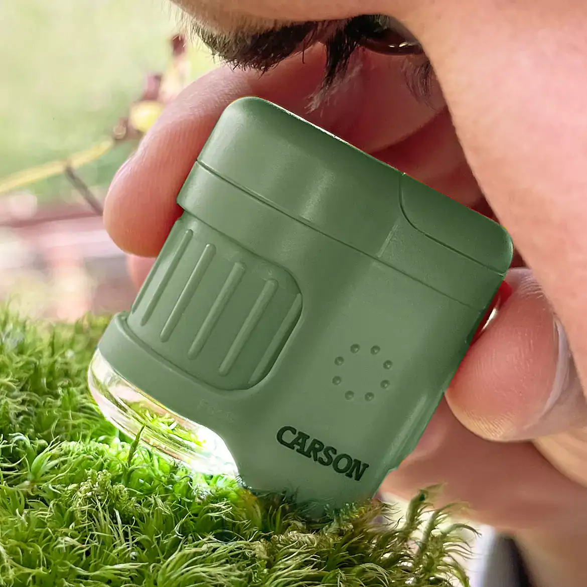 Una persona debe observar cerca con el Microscopio de bolsillo Carson MM-280G MicroMini™ 20x, color verde, sosteniéndolo junto a su ojo.